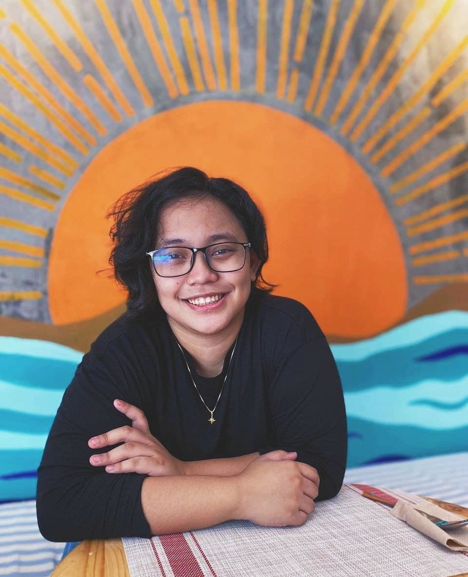 Joal smiling at a café table in front of a painted sunset mural
